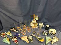 Full display shot of all items including glassware, mugs on rack, ceramic items, fabric scissor holders, and metal coasters