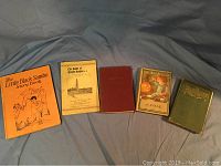 Five vintage books arranged side by side on a cloth: including two copies of The Little Black Sambo Story Book, a small softcover pamphlet titled 'The Battle of Groton Heights', and two hardback books with embossed covers and illustrated dust jackets.