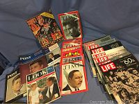 Photo showing a stack of vintage magazines laid out on a blue cloth background featuring Post, Time, Look, and Life titles with covers showing JFK, Martin Luther King, and Beatles related images.