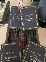 Box with multiple vintage hardcover books, labeled 'Great Men and Famous Women' with black covers and gold lettering, stacked with other old hardback books visible inside.