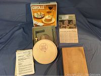 Full set laid out including box, clamp arm, stone base, cutting board, instruction manual, and newspaper article.