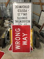 Photo showing several stacked metal street signs with the 'Wrong Way' sign in front and a large white residential notice sign visible in the back.