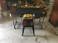 Desk viewed from front with chair placed in front and some items on chair seat (not included). Desk has metal legs and wooden top with black desk pad.