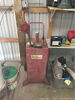 Full front view of the red 30 gallon gas caddy showing the main tank body, pump with crank handle (broken), and handle on back for transport.