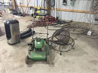 John Deere green push mower and black metal firepit with round shape seen from the front in a garage.