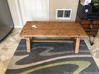 Coffee table angled front view showing legs and stretcher on a patterned rug against a wall.