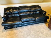 Front and side view of black leather-look sofa showing wear and tear, leather creases, and missing legs.