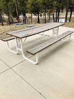 Full view of the wooden picnic table outdoors on a cement slab, showing the table top and benches attached to white metal supports.