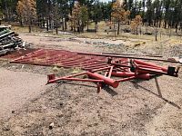 Wide view of disassembled red cattle guard parts lying on ground showing tubular rails and support braces