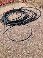 Photo of multiple lengths of coiled black plastic tubing on a paved surface, showing different diameters and lengths.