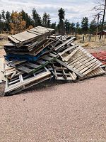 Piles of wooden pallets outdoors, showing mix of whole and broken pallets, some painted blue or red, others natural wood color