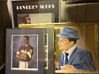 Photo showing two framed signed Art Monk photos and Frank Sinatra canvas painting, plus a framed 'Poverty Sucks' photo behind.
