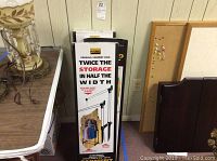 Three boxed new parallel garment rolling racks stacked vertically by a table and bulletin board.