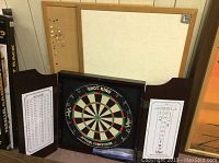 Red oak dartboard case containing the dartboard and dry erase side scoreboards, with two cork boards behind it.