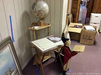 Photo showing bamboo corner shelf with the globe placed on top, wooden table under the butler tray holder and a framed painting on the floor nearby.