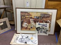 Framed artwork with a vintage baseball batter scene and three items displayed in front: calendar, cartoon sketch, and calendar cover