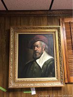 Framed portrait of a man in a red beret and green coat, in a carved gold-toned wooden frame.