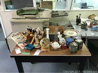 Table with multiple decorative items: several glass bud vases, figurines, plates, and Christmas ornaments.