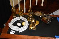 Full lot photograph showing brass busts, brass animals, porcelain decor pieces, egg-shaped paperweights, brass ashtray, and small brass cannon.