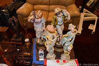 Photo of four ceramic statues on table in front of leather couch, two Yankee-style 24 inch and two Asian-style 20 inch figurines