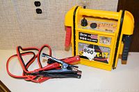 Yellow Vector portable car battery charger with red and black jumper cables coiled next to it.