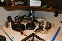 Countertop with stainless steel teapot, several metal pots and pans, blender in background, glass baking dish