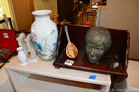 Wooden shelf showing Asian vase, head sculpture, miniature string instrument, and horse head bookends with carved horn on right side