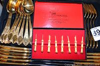 Close-up of gold-tone spoons, forks, and original red velvet lined box containing 8 gold-toned corn on the cob forks with bamboo-style handles