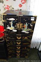 Full view of the black dresser showing Asian artistic details, brass hardware, and multiple drawers.