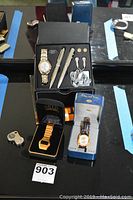 Top overview of the watches, pens, cufflinks and accessories arranged on a black glass surface, showing all items in the lot.
