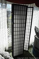 Front view of a three-panel room divider screen with wooden grid and white translucent rice paper panels, shown indoors in front of lace curtains.