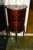 Front view of semi-circular wooden jewelry dresser with five drawers and brass hardware.