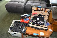 Wide view of the lot showing a black molded case with socket tools, black hand tool case with various tools inside and on holders, and small hardware bags