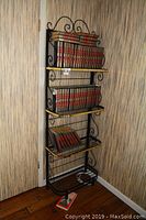 Full view of the black metal bakers rack with golden accents and books arranged on four shelves.