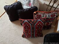 Four pillows including two black pillows and two with colorful intricate embroidered patterns in reds and blues