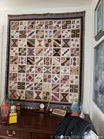 Frontal photo of Peruvian rug with geometric patterned squares hung on a wall above a wooden desk with small trophies and framed pictures.