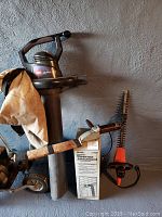 Photo shows vintage Weed Eater trimmer with large cylindrical base and a protective beige cloth bag, Toro leaf blower with black and orange casing and two pairs of hedge clippers with wooden and orange handles, against a textured wall.