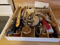 Top view of a compartmentalized tray holding multiple scissors, knives, pliers, metal jar lids and various small tools showing wear and age.