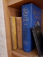 Four books side by side on a wooden shelf: The Willow Whistle (yellow), Recipe Book (brown), What a Boy Saw in the Army (blue), French West Pocket Dictionary (black).