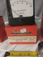 Simpson Model 1327T taut band panel meter on top of its original red box with measurement for scale