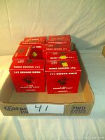Twelve Ademco 747 Indoor Sirens in their original red boxes stacked in two rows within a cardboard tray labeled 'Corona Extra Two 12 Packs'. Boxes are visibly labeled with product name and brand.