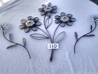 Top-down photo showing the entire metal wall art piece with three large flowers and one smaller flower on a white tablecloth.