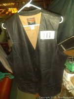 Front view of black leather vest hanging on a white hanger, showing its sleeveless design and front pockets.