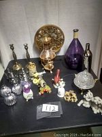 Full view of assortment on table showing brass candle holders, glass bottles, ceramic and plush figurines