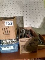 Boxes and container filled with different peg board hooks of various sizes and materials arranged in front of a peg board wall.