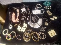 Photo showing a variety of costume jewelry including necklaces, bracelets, earrings, and rings arranged on a white cloth.