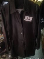 Front view of black leather coat on hanger with button closure and collar, marked with lot number tag.