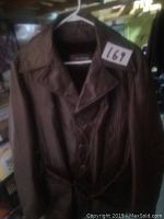 Full view of the brown leather coat hanging on a white plastic hanger, showing fron button closure and belt.