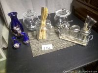 Overview of assortment on black surface including blue floral vases, glass jars with lids, two jars with knob handles, and a metal and wood condiment holder