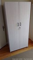 Front view of tall light wood cabinet with closed double doors and lock